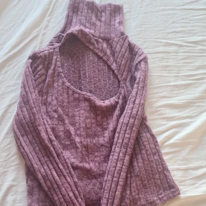 Lila ribbad polotröja - Säljer en snygg lila ribbad polotröja med lång ärm och en unik öppen rygg. Perfekt för att hålla stilen under kyligare dagar. Passar bra till både jeans och kjol.
