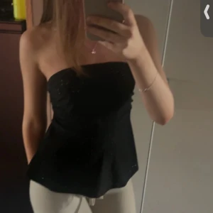 Svart axelbandslös tubtopp - Snygg svart axelbandslös tubtopp med volangkjol. Har aldrig använts💕