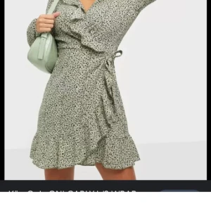 Grön prickig omlottklänning - Snygg grön omlottklänning från ONLY (Nelly) med prickigt mönster och volangdetaljer. Klänningen har långa ärmar och knytband i midjan för en smickrande passform. Perfekt för en stilfull look.