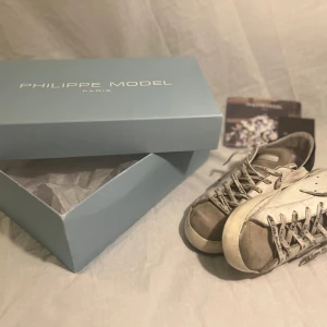Grå sneakers från Philippe Model - Snygga grå sneakers från Philippe Model med snörning och en stilren design. Skorna har en kombination av olika grå nyanser och vita detaljer, vilket ger dem en modern look. Perfekta för en avslappnad stil. 