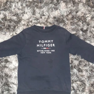 Mörkblå sweatshirt från Tommy Hilfiger - Säljer en stilren mörkblå sweatshirt från Tommy Hilfiger med deras ikoniska logga på bröstet. Tröjan har långa ärmar och ribbade muddar vid ärmslut och nederkant. Perfekt för en casual look!