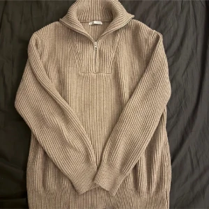 Beige ribbad tröja från Zara - Säljer en stilren beige ribbad tröja från Zara med dragkedja vid halsen. Tröjan har långa ärmar och en hög krage som ger extra värme. Perfekt för kyligare dagar! Sitter mer som S