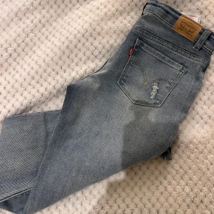 Lågmidjade jeans från Levi's - Snygga lågmidjade blå jeans från Levi's med en klassisk femficksdesign och slitna detaljer. De har en bekväm passform och Levi's-loggan syns tydligt på bakfickan.