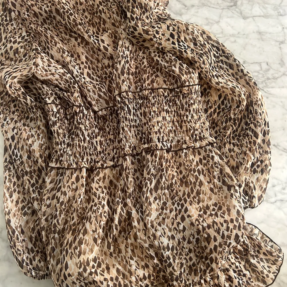 Snygg leopardmönstrad klänning från Zara med smockdetaljer i midjan. Klänningen har långa ärmar och en knytning vid halsen. Perfekt för en trendig sommarlook! Passar s-m. Använd en gång. . Mekot.