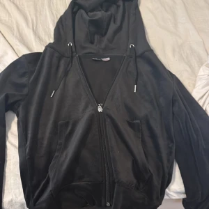 Svart hoodie från Gina Tricot - Säljer en svart hoodie från Gina Tricot med dragkedja och huva. Den har långa ärmar och dragsko vid huvan för justering. Perfekt för en avslappnad stil.