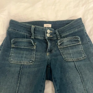 Blå jeans från Nelly - Snygga blå jeans från Nelly med bootcut-stil och låg midha. De har dubbla knappar fram och praktiska fickor både fram och bak. Perfekta för en avslappnad look. Nypris 699, använda ett fåtal gånger 