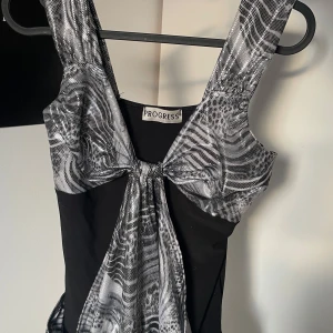 silver black top - Snygg svart topp med silvermönstrade detaljer från Progress. toppen har ett unikt mönster och en knytning framtill som ger en elegant touch. Perfekt för en kväll ute eller en speciell tillställning. tyvärr inte mycket utrymme för större bröst :(💕