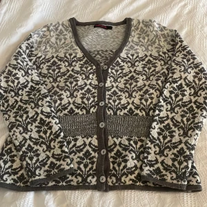 Mönstrad kofta från Indiska - Säljer en snygg mönstrad kofta från Indiska i grått och vitt. Koftan har långa ärmar och knappar framtill. Perfekt för kyliga dagar med sitt stickade material och stilrena design.Känns mera som M i storlek.