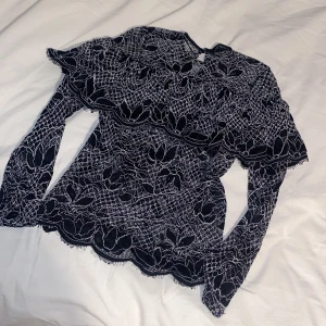 Svart zara spetsblus - Elegant svart spetsblus med vackert blommönster. Blusen har långa ärmar och en hög hals, perfekt för en stilfull look. Den har en fin struktur och detaljer som ger en lyxig känsla.