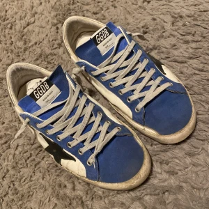 Golden goose skor - Snygga sneakers från Golden goose i blått, svart och vitt. Skorna har snörning och en fet röd sula. Perfekta för en avslappnad stil. Lite trasiga sulor men inget som märks direkt när de används.