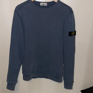 Blå sweatshirt från Stone Island - Säljer en blå sweatshirt från Stone Island Junior med deras ikoniska märke på ärmen. Tröjan har långa ärmar och en klassisk rund halsringning. Perfekt för en stilren och avslappnad look. Priset är inte hugget i sten kom med prisförslag!