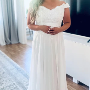 Bröllopsklänning/ Brudklänning - Elegant brudklänning med hjärtformad urringning och spetsdetaljer upptill och ett flytande, lätt tyg. Storlek L enl lappen men mer som M. Aldrig använd. inköpt på butik i Örebro augusti -24. Lapp på klänning är kvar. (Obs:På de två sista bilderna ser tyger mörkare ut eftersom jag har svarta strumpbyxor på)