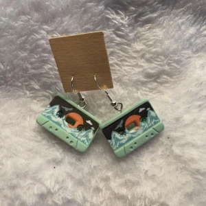 Handgjorda örhängen med landskapsmotiv - Unika örhängen i form av små kassettband med motiv av berg, solnedgång och vatten. Färgerna är mintgrön, svart, vit och orange. Perfekta för dig som gillar naturinspirerade accessoarer. Krokarna är i sterling silver