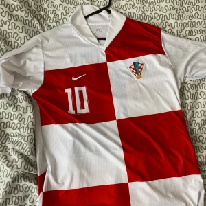 Kroatien fotbollströja Nike - Säljer en klassisk Kroatien fotbollströja från Nike med rödvita rutor och nummer 10 på bröstet. Tröjan har korta ärmar och Kroatiens landslagsemblem på vänster sida. Perfekt för fotbollsfans! Modric 10 XXL men passar XL