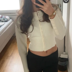 Vit croppad kofta med knappar - Säljer en vit croppad kofta med långa ärmar och knappar framtill. Tröjan har en tight passform och är ribbad i materialet vilket ger en snygg och modern look.