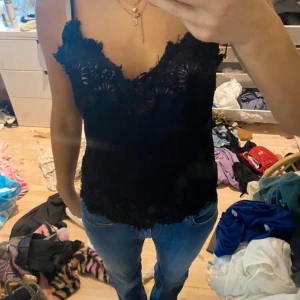 Svart linnetopp med spetsdetaljer - Säljer en svart linnetopp med fina spetsdetaljer längs urringningen och nederkanten. Perfekt att styla till jeans eller kjol. Den är dock lite sliten!💕