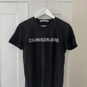 Svart t-shirt från Calvin Klein Jeans - Svart t-shirt från Calvin Klein Jeans med vit logga tryckt över bröstet. Klassisk rund halsringning och korta ärmar. Tillverkad i mjuk bomull för en skön känsla och enkel stil.