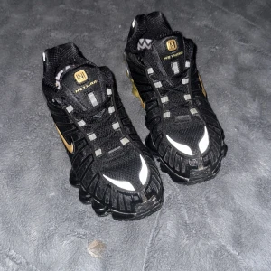 Nike Shox TL Neymar Edition - Säljer ett par svarta Nike Shox TL Neymar Edition med guldiga detaljer och reflekterande inslag. Skorna har en unik fjädrande sula och mesh-överdel för bra ventilation. Perfekta för dig som vill sticka ut med en sportig och modern look. Säljer för de är för små.