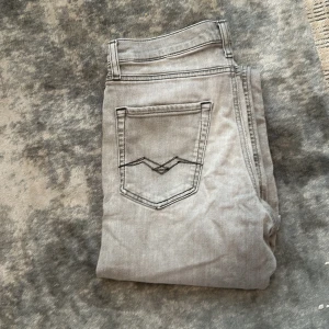 Ljusgrå jeansbyxor från Replay - Säljer ett par ljusgrå jeansbyxor från Replay med klassisk femficksdesign och raka ben. Byxorna har tydliga sömmar på bakfickorna och en snygg Replay-patch i midjan. Perfekta för dig som gillar stilrena och enkla jeans.