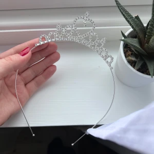 Silverfärgad tiara med strass - Säljer en glittrig tiara i silverfärg med dekorativa hjärtan och gnistrande stenar. Perfekt accessoar för fest eller bal. Sitter bekvämt på huvudet med tunn metallram. Önskar du veta exakta mått? Tveka inte att höra av dig!
