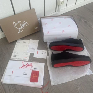 Christian Louboutin skor  - Säljer ett par svarta sneakers från Christian Louboutin med ikoniska röda sulor och svarta nitar framtill. Skorna har snörning och är tillverkade i mocka med lyxig känsla. Perfekta för dig som vill sticka ut med exklusiv design. Allt OG följer såklart! Helt nya🙌🏼✅ skriv vid funderingar!