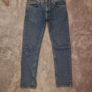 Blå jeansbyxor från Nudie Jeans - Klassiska blå jeans från Nudie Jeans med rak passform och normal midja. Jeansen har fem fickor och tydliga sömmar på bakfickorna. Tillverkade i slitstarkt denimtyg och passar perfekt till en avslappnad stil.