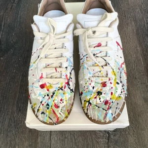Maison Margiela paintsplater - Unika vita sneakers från Maison Margiela med färgstänk i rött, blått, gult, svart och grönt. Skorna har snörning, rund tå och platt sula. Snygg konstnärlig look och bruna yttersulor. Perfekta för dig som vill sticka ut med din stil. Skorna är i extremt bra skick tvättas självklart innan frakt. Box och sko påsarna medföljer. Kan gå ner i pris vid snabb och smidig affär. 