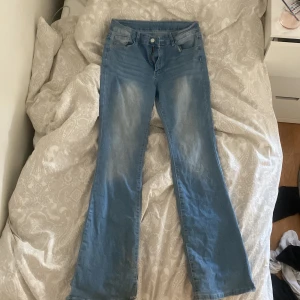 Blå bootcut jeans med broderade bakfickor - Säljer ett par ljusblå bootcut jeans med snygga broderade detaljer på bakfickorna och klassisk femficksdesign. Jeansen har normal passform och är tillverkade i denim med lätt slitning framtill. De är köpta i storlek L men passar både L & M