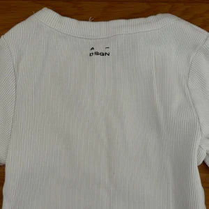 Vit ribbad långärmad topp från A DSGN - Säljer en vit ribbad långärmad topp från A DSGN. Tröjan har en tight passform och är tillverkad i ett mjukt, stretchigt material. Perfekt att styla med jeans eller kjol för en clean look. Den enda defekten är att lappen är lite trasig som ni kan se i sista bilden