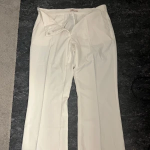Vita kostymbyxor från Nelly - Säljer ett par vita kostymbyxor från Nelly med boot cut och är lowaist midja. Byxorna har diskreta fickor bak och stängs med dragkedja och knapp framtill. Perfekta för en stilren look. Säljer då de ej passar:)