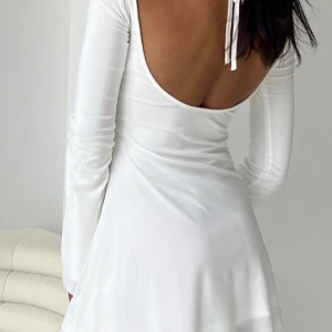 Vit långärmad klänning med öppen rygg - Säljer en stilren vit klänning med lång ärm och snyggt öppen rygg. Klänningen har en lätt utsvängd ärm och är tillverkad i ett mjukt, följsamt material. Perfekt för dig som vill ha en enkel men elegant look.
