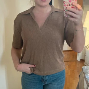 Beige stickad polotopp - Brun tröja från H&M i strukturmönstrad trikå med lös passform, krage & korta ärmar. Fint skick. Storlek S vilket på H&M motsvarar 38 🤎