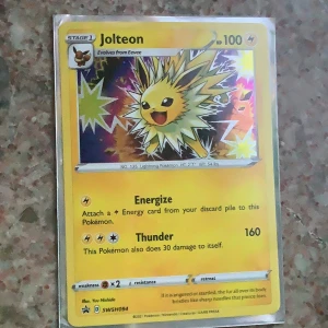 Jolteon Pokémonkort - Jolteon holografiskt samlarkort från Pokémon. Kortet har gul ram, glittrig bakgrund och visar Jolteon i en elektrisk pose. HP 100, attackerna Energize och Thunder. Perfekt för samlare eller Pokémonfans.
