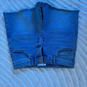 Blå jeansshorts med rå kant - Säljer ett par blå jeansshorts från name it med rå, fransad kant upptill. Shortsen har klassiska fickor fram och bak samt knapp och dragkedja. Perfekta för sommaren och ger en avslappnad look. De är i barnstorlek 158 men de är väldigt stretchiga och passar mig som har S