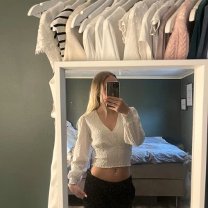 Vit croppad blus med v-ringning - Säljer en vit croppad blus med v-ringning och långa ärmar. Blusen har en lätt rynkad struktur och är perfekt för dig som vill ha en stilren och trendig topp. Passar till både jeans och kjol. Toppen är liten i storleken och passar för dem som har S