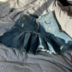 Jeanskjol med volang och slitningar - Säljer en blå jeanskjol med volang och råa kanter. Kjolen har flera slitningar och en markerad söm som delar av över- och underdel. Klassisk femficksmodell med dragkedja och knapp framtill. Från shein, väldigt liten i storleken. Gissningsvis passar den S/liten medium.