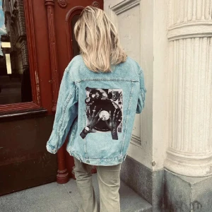 Ljusblå jeansjacka med tryck på ryggen - Jättesnygg jeansjacka med tryck på ryggen. Är köpt från JaquiUF och är oanvänd! Ärmlängd (från armhåla):44cm Byst:57cm Längd:69cm Sorlek: L Modellen är 167cm