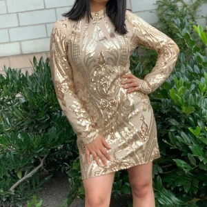 Guldig paljettklänning med lång ärm - Säljer en glittrig guldig klänning med lång ärm och höghalsad design. Är storlek M men passar också i S