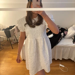 Studentklänning - Superfin vit kortklänning från BYIC i modellen Edith Dress. Klänningen har puffärmar, strukturmönster i tyget och dragkedja bak. Perfekt för student eller sommarens alla tillfällen. Säljes med lapp kvar och är endast testad.