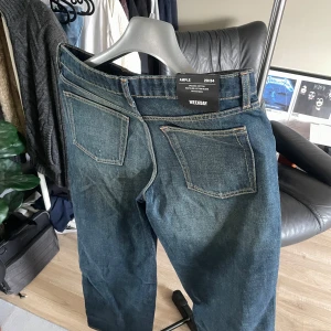 Blå loose fit jeans från Weekday - Säljer ett par blå jeans från Weekday i modellen Ample. Jeansen har loose fit, raka ben och klassiska bakfickor. Tillverkade i en blandning av ekologisk och återvunnen bomull. Perfekta för en avslappnad stil. Riktigt schysst fade över benen