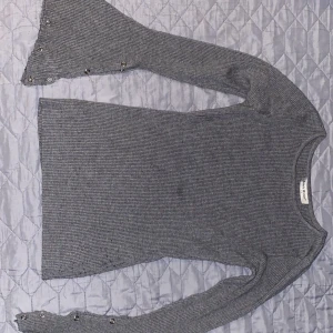 Grå ribbad tröja med utsvängda ärmar från Beauty Women - Säljer en grå ribbad tröja från Beauty Women i storlek S/M. Tröjan har långa, utsvängda ärmar med dekorativa knappar längs ärmsluten. Perfekt för dig som gillar unika detaljer och en trendig look.