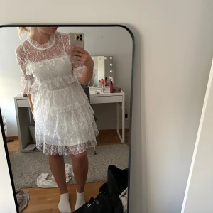 Vit spetsklänning med volanger - Superfin vit kortklänning i spets med volanger. Perfekt för somriga tillfällen eller studentfirande. Liknar by malina klänningen. Helt ny. Med prislapp kvar.