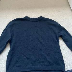 Mörkblå stickad tröja - En enkel och stilren mörkblå stickad tröja med rund halsringning. Perfekt att matcha med jeans eller kjol för en avslappnad look. Tröjan har långa ärmar och ribbade muddar vid ärmslut och nederkant. Storlek 160