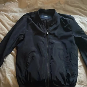 Svart bomberjacka från ONLY - Säljer en svart bomberjacka från ONLY i storlek S. Jackan har dragkedja framtill, två snedställda fickor och ribbade muddar vid ärmslut och nederkant. Perfekt för en stilren och enkel look.