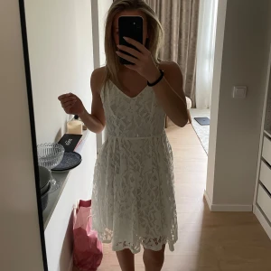 Vit spetsklänning med v-ringning - Säljer en vit klänning i ett fint spetsmönster med smala axelband. Klänningen är från NA-KD i storleken 34. Endast använd ett fåtal gånger och har inga tecken på användning🌺
