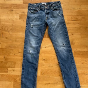 Blå slim fit jeans från Jack & Jones - Säljer ett par blå slim fit jeans från Jack & Jones, modell Slim/Glenn. Jeansen har slitna detaljer och klassisk femficksdesign. Perfekta för dig som gillar en smalare passform och en lite ruffare look.