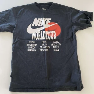 Svart Nike World Tour t-shirt - Säljer en svart Nike t-shirt med stort tryck framtill: 'Nike World Tour' och namn på olika städer. Klassisk passform och rund halsringning. Perfekt för dig som gillar streetwear och sportig stil. Pris kan diskuteras vid snabb affär!