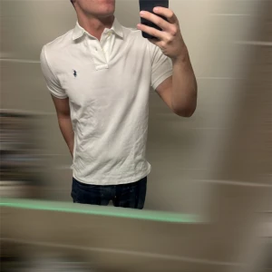 Ralph Lauren Piké  - Säljer en klassisk vit pikétröja från Ralph Lauren med den ikoniska loggan broderad på bröstet. Tröjan har korta ärmar och en stilren krage med knappar. Perfekt för en avslappnad men ändå stilren look. Modellen på bild är 180 o väger 71kg