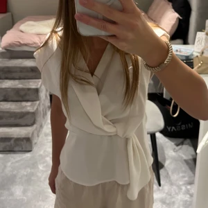 Vit omlottblus med knyt - Säljer en stilren vit omlottblus med knyt i midjan. Blusen har korta ärmar och en v-ringad omlottdesign som ger en elegant look. 