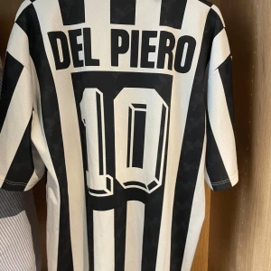 Juventus fotbollströja Del Piero 10 - Klassisk Juventus fotbollströja med svartvita ränder, Del Piero och nummer 10 på ryggen. Den är köpt av farsan för flera år sedan och har inte använts, har bara legat i garderoben och väntat på att den ska passa i storleken. Hör av er om ni undrar något eller kolla mina andra plagg!!✅✅